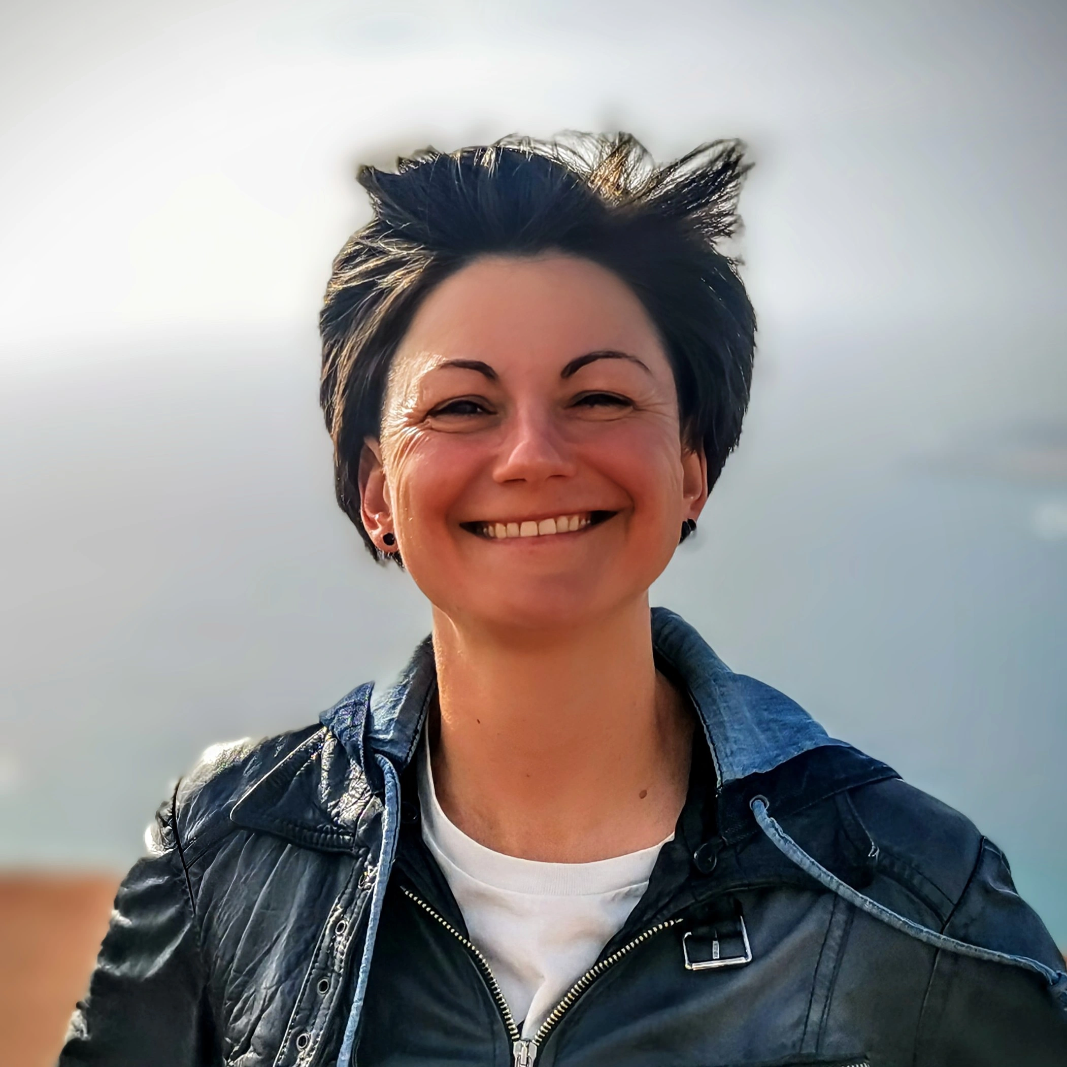Porträt von Sandra Grösch, Gründerin von Die Queere Finanzberatung, lachend mit wehenden Haaren und Lederjacke